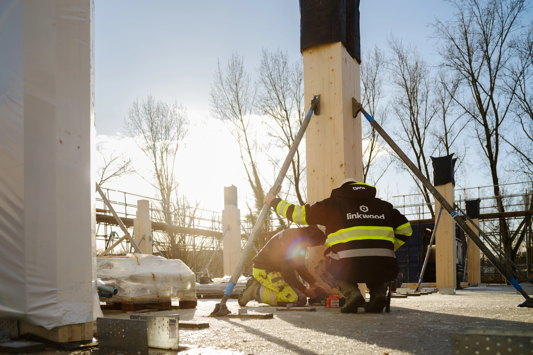 medewerker bevestigt een houten kolom met een stelstang in de zon