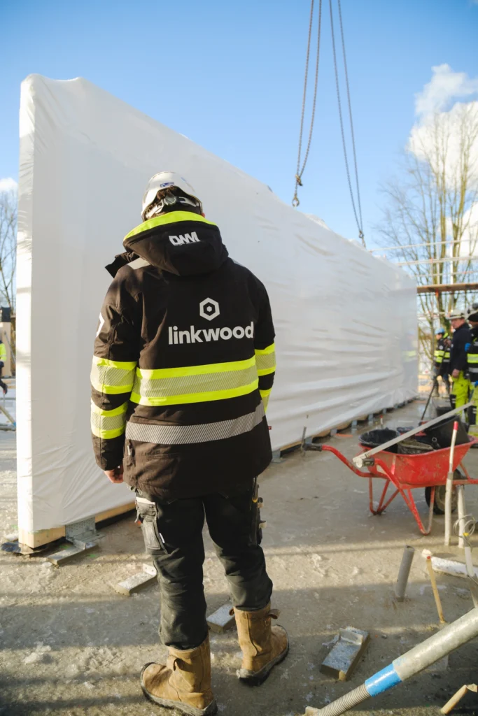 medewerker met linkwood jas kijkt naar het ingepakte houten wandelement dat wordt aangevoerd