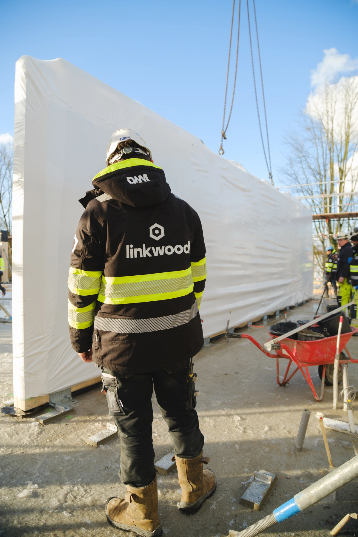 medewerker met linkwood jas kijkt naar het ingepakte houten wandelement dat wordt aangevoerd