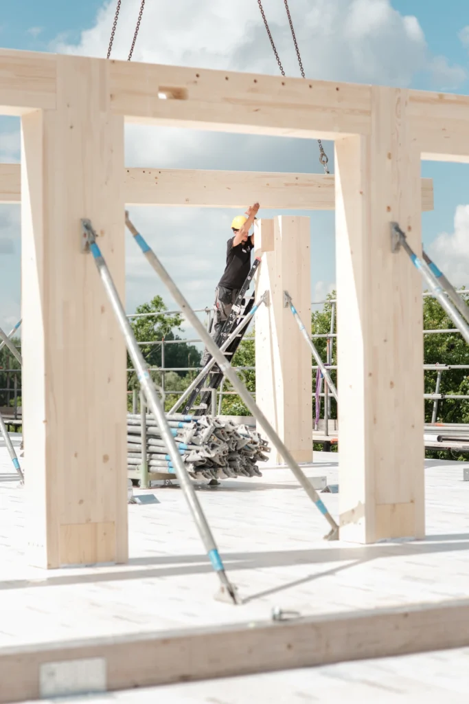 medewerker op een ladder bevestigt een houten kolom onder een hangende balk