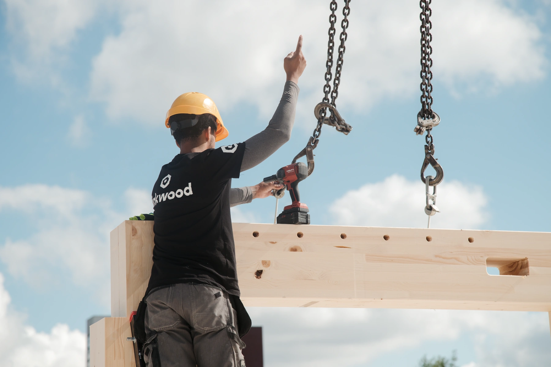 medewerkerseint naar de kraanmachinist terwijl hij een houten balk op de goede plek laat zakken