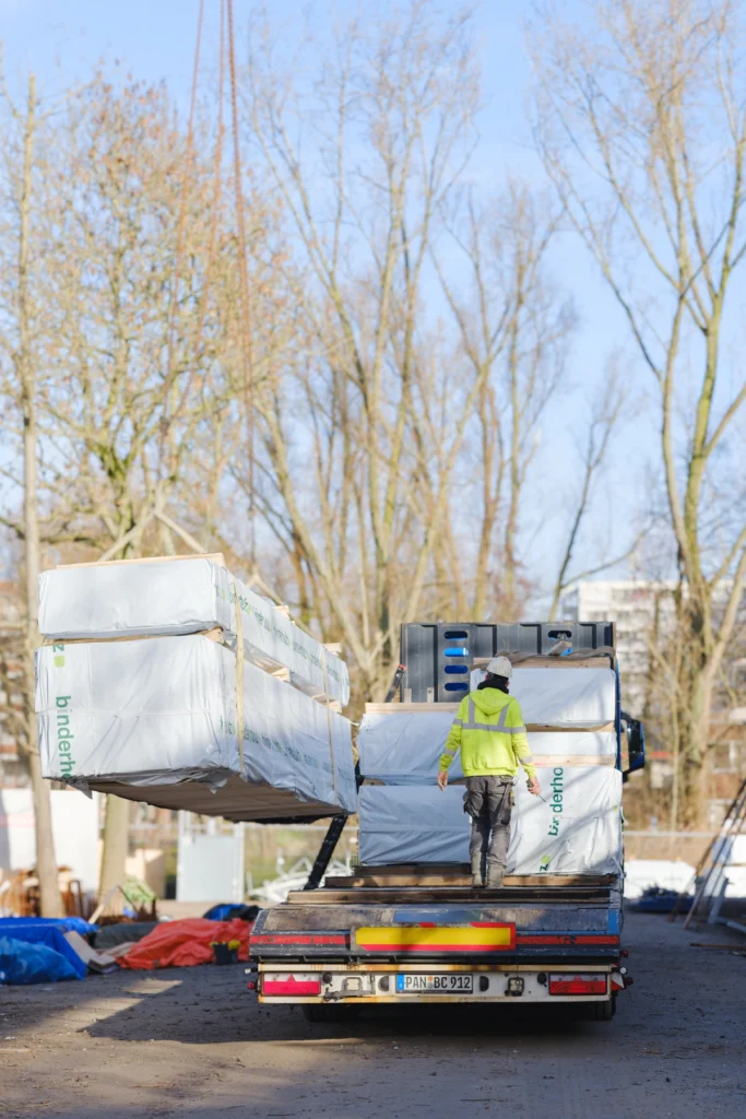 vrachtwagen met verpakte houten bouwelementen wordt gelost op de bouwplaats